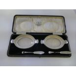 A silver salt set cased by Stokes and Ireland Ltd with glass insets and ball feet, having oval form.