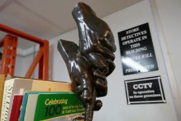 A modern bronze sculpture of hands pulling rope
