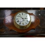 An old brass ship's bulkhead clock on shaped mahogany plaque