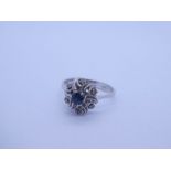 18K white gold dress ring with central round cut sapphire on a floral design mount inset small diamo