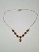 14ct gold necklace with articulated floral panels each set with an oval faceted garnet and central s