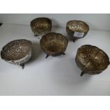 A set of five white metal bowls with a scalloped design edge, chased flower body and three feet in t