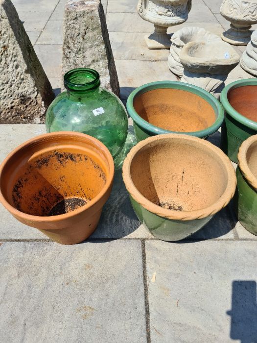 A green glass carboy and other garden pots