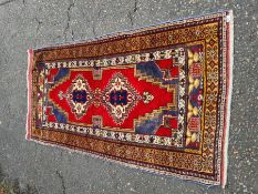 A Caucasian style rug having 2 central diamond motifs in a red field, 200 x 102cm