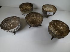 A set of five white metal bowls with a scalloped design edge, chased flower body and three feet in t