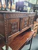 An antique oak coffer having carved panelled front, (one leg replaced)