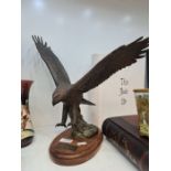 A modern bronze sculpture of eagle in flight on oval wooden plaque