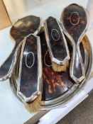 A silver and tortoise shell dressing table set comprising of three brushes, a hand mirror and a tray