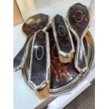 A silver and tortoise shell dressing table set comprising of three brushes, a hand mirror and a tray