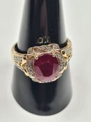 Contemporary dress ring with central oval faceted ruby surrounded diamond chips and into split shoul
