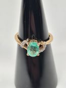 9ct yellow gold dress ring with oval cut central emerald, and split shoulders set with zircons, size
