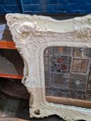 An antique style cream painted wall mirror, having scroll decoration with bevelled glass