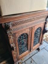 A carved wooden cupboard depicting lion masks with stained glass doors