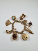 Heavy 9ct yellow gold charm bracelet hung with 8 charms including a fan, sewing machine, garnet set