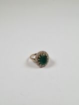 Unmarked white gold dress ring with central oval mixed cut emerald, surrounded 12 round cut diamonds