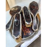 A silver and tortoise shell dressing table set comprising of three brushes, a hand mirror and a tray