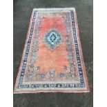 A Turkish rug woven with central oval blue floral medallion on pink field framed by floral border,