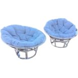 A pair of circular cane conservatory chairs with loose cushions on bowl shaped seats, raised on