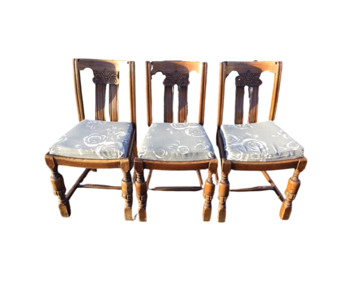 A set of three oak chairs with scroll carved backs and cushion seats, raised on turned legs joined