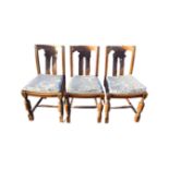 A set of three oak chairs with scroll carved backs and cushion seats, raised on turned legs joined