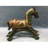 A painted carved hardwood toy horse inlaid with brass banding, on arched wheeled support. (15.75in)