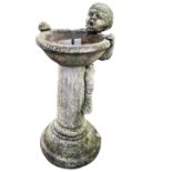 A composition stone garden birdbath fountain with ribbed column beneath circular bowl, with small