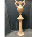 An internally illuminated carved alabaster column lamp with urn shaped vessel having stylised horned