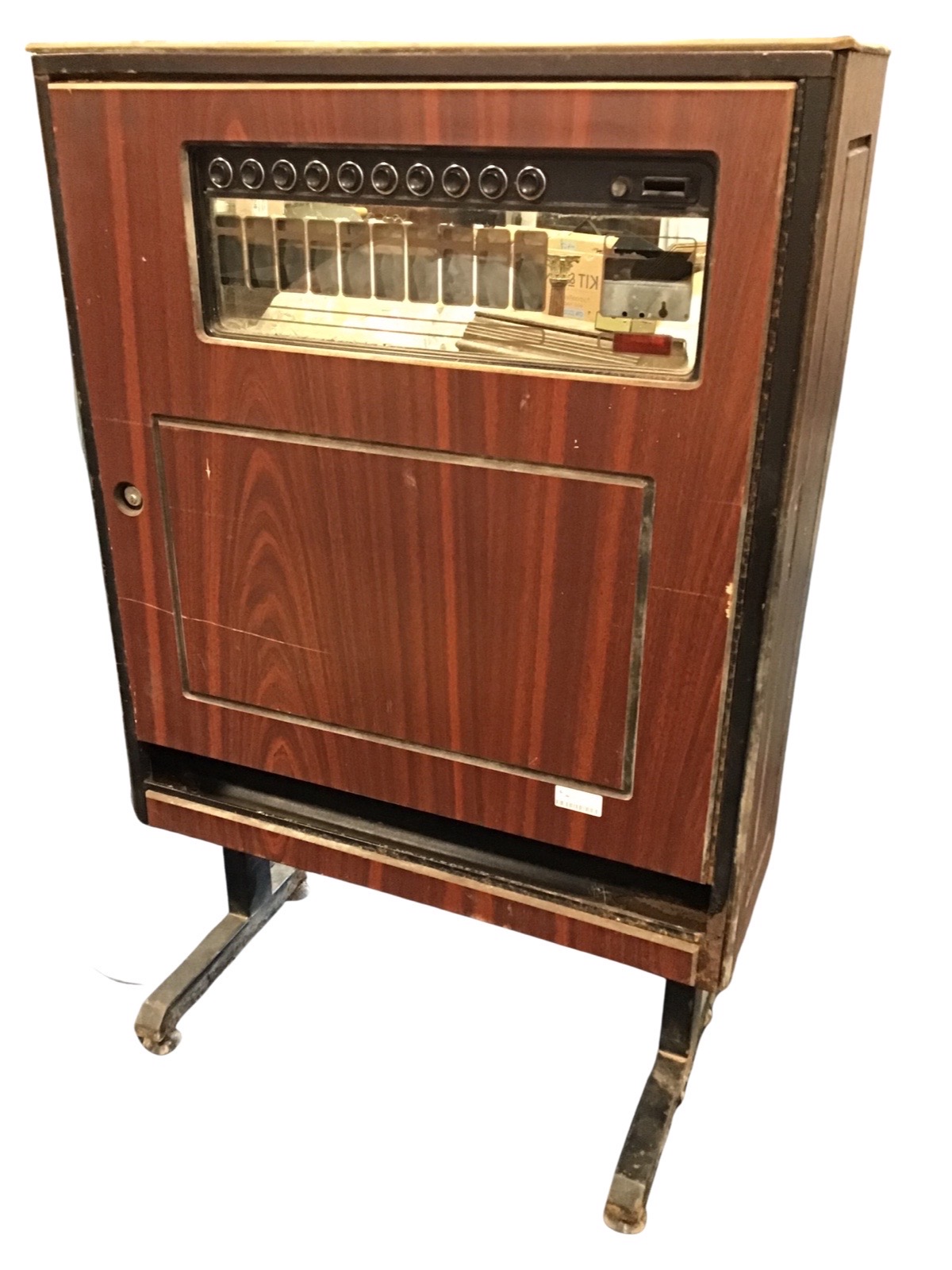 A cigarette vending machine with glass panel in hinged locking door with dispensing trough below,