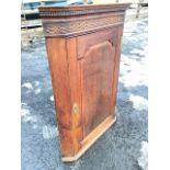 A Georgian oak corner cabinet with moulded ogee cornice framing a greek key band above a blind