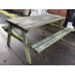 A garden table with integral batton bench seat, the table with slatted top supported on bolted