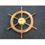 A mahogany ships wheel with dowel jointed turned spindles centering on a brass faced clock by The