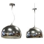 A pair of contemporary hanging lights with chromed bowl shaped shades suspended from bun shaped