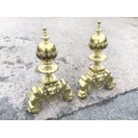 A pair of nineteenth century large brass firedogs, with urn shaped lobbed finials above scalloped