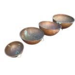 A graduated set of circular copper bowls, the hammered vessels with rolled rims mounted with brass
