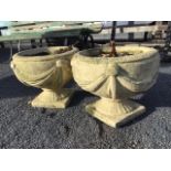 A pair of composition stone garden urns cast with swagged draped style decoration to bulbous pots on
