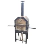 A garden BBQ oven with tubular chimney above two drop-down doors, having two hinged shelves to