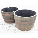 A pair of oak garden barrel tubs, each having staves framed by three riveted metal strap bands. (