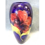 A tall Moorcroft tube lined vase decorated with flowers and leaves on cobalt blue brushwork ground -