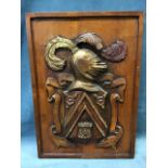 A rectangular carved hardwood panel depicting an amoral crest with plumed helmet above shield,