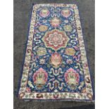 A Wilton style rug woven with floral medallions on blue field with scrolling, framed by ivory border