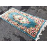 A thick pile wool rug woven with oval floral medallion and frieze on turquoise ground, with fringe