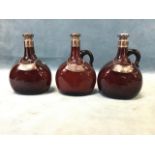A set of three ruby glass flask shaped decanters with labels for gin, whiskey and brandy, having