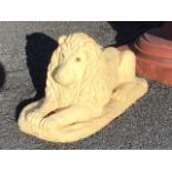 A painted composition stone garden lion, the beast with glass eyes lying in prone position on