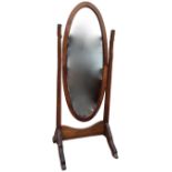 An oval mahogany cheval mirror with boxwood strung inlaid decoration, the bevelled plate supported