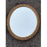 An oval wall mirror, the plate in pierced leaf scrolled composition frame with ribbon moulded