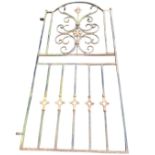 An arched wrought iron garden gate with foliate scrolled panel flanked by square pillared frame with
