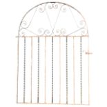 An arched wrought iron garden gate with scrolled decoration to top panel, above twisted and square