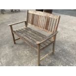 A hardwood garden bench with arched slatted panel to back, having tapering platform arms on
