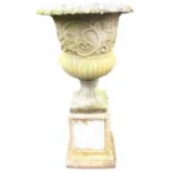 A composition stone garden urn on stand with lozenge moulded rim above foliate cast frieze, the