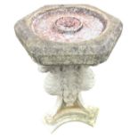A composition stone garden birdbath with hexagonal bowl supported by three gryphons on paw feet,